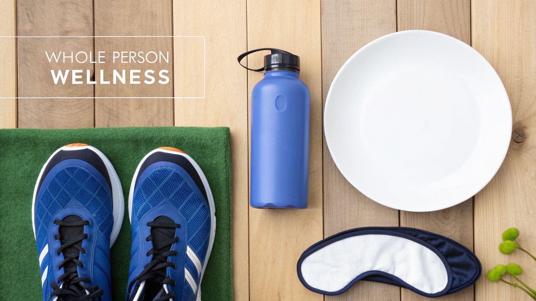 A flat lay of wellness items including athletic shoes, water bottle, plate, eye mask, and plants on wood.
